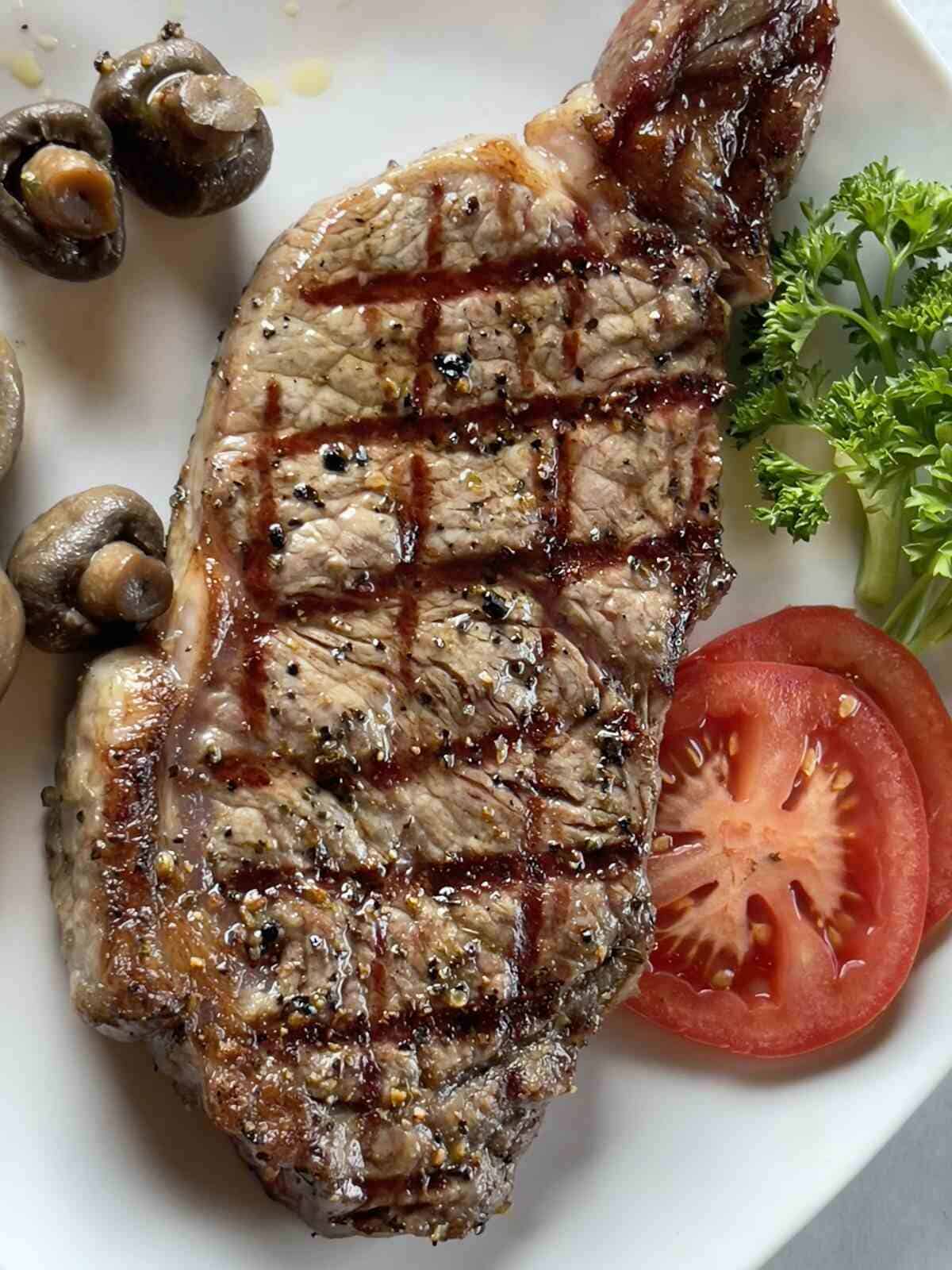 A perfectly grilled New York Strip steak served with mushrooms, fresh tomato slices, and garnished with broccoli at River Lake Inn Restaurant.